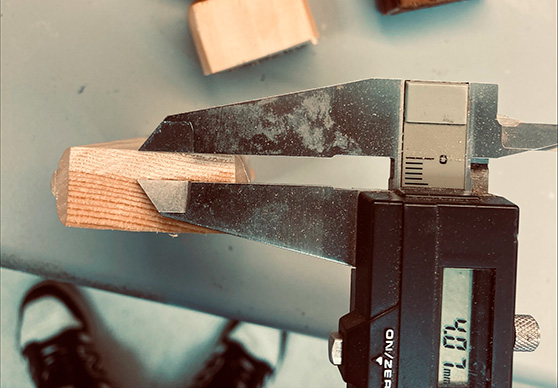 Digital callipers measuring the thickness of a small wood sample in a laboratory.