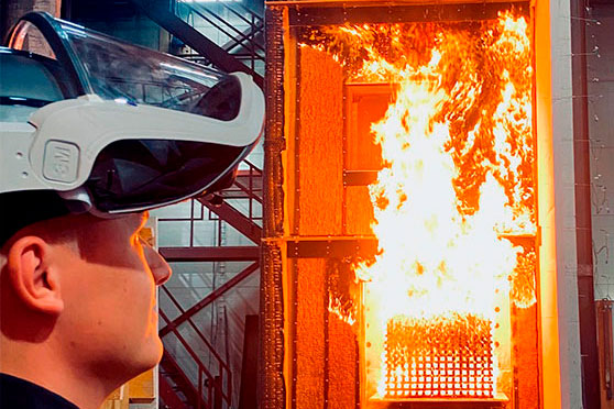 Person wearing a protective visor observing a full-scale fire test of a facade element in DBI’s test hall.