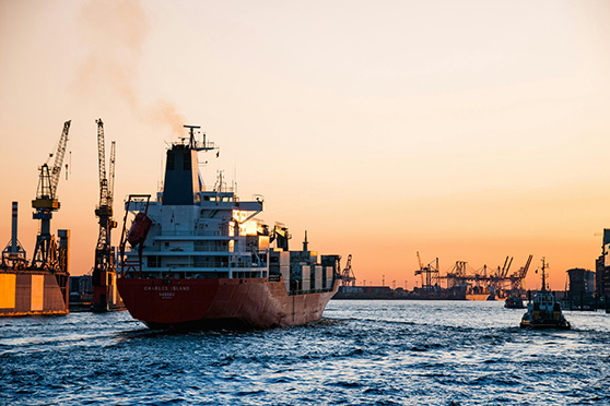 Cargo ship sailing through a harbour at sunset.