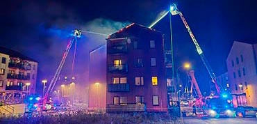 Two aerial ladders spraying water onto the roof of a burning apartment building in Upplands-Bro.