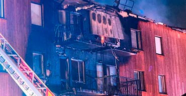 Fire-damaged timber facade with severely damaged balconies and roof structure in Upplands-Bro.