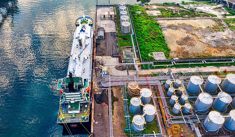 Aerial view of a tanker moored beside storage tanks and pipelines at a port terminal.
